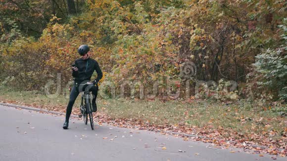 穿着黑色自行车服装和头盔的职业男子自行车运动员开始在公路自行车上训练年轻迷人的铁人三项视频的预览图