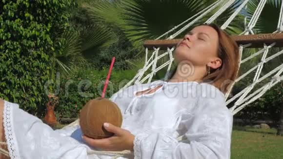 年轻女子躺在吊床上用椰子水鸡尾酒视频的预览图