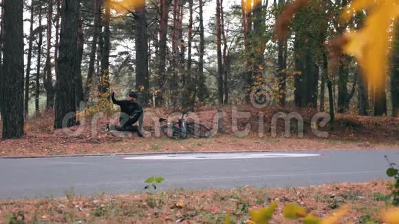 快乐的年轻职业男运动员穿着黑色自行车装备坐在秋天的公园里在电话和drin上自拍或拍照视频的预览图