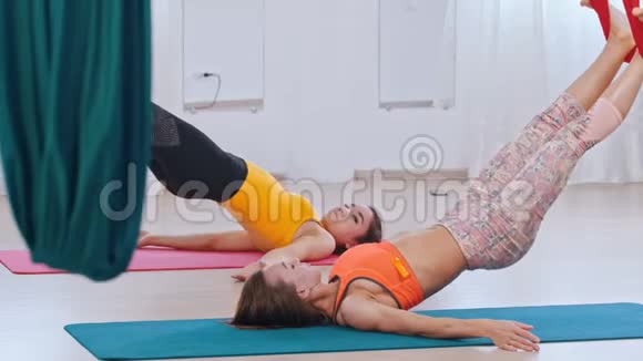 空中瑜伽两个女人做运动躺在垫子上双腿挂在吊床上视频的预览图