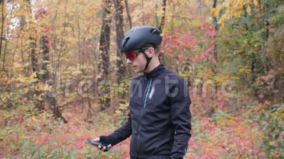 在秋季城市公园的智能手机上自拍的骑自行车服装的年轻迷人的Sports家伙拍摄照片的专业自行车手视频的预览图
