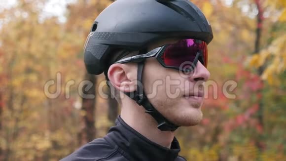 年轻英俊的职业三项运动员戴着黑色头盔和自行车手套在秋季公园摘下运动眼镜的肖像额外费用视频的预览图