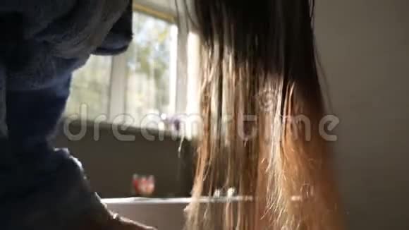 布鲁内特女孩吹干湿发背景下的太阳光线靠近窗户女人正在给头发做造型视频的预览图