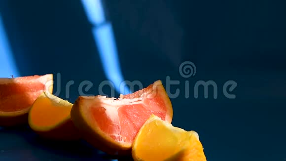 在蓝色背景上切片的柑橘类水果葡萄柚和橘子阳光下有很深的阴影视频的预览图