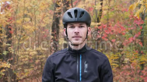 迷人的男性自行车手黑色头盔和温暖的热运动装站在秋季城市公园并戴上运动眼镜肖像视频的预览图