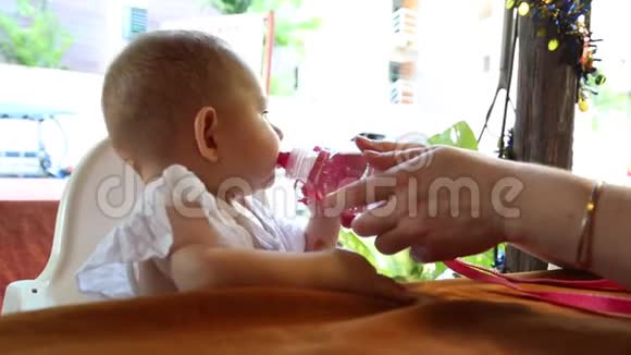 妈妈给一个婴儿喝一杯他坐在户外咖啡馆的一张桌子上坐在一个特殊的儿童座位上视频的预览图