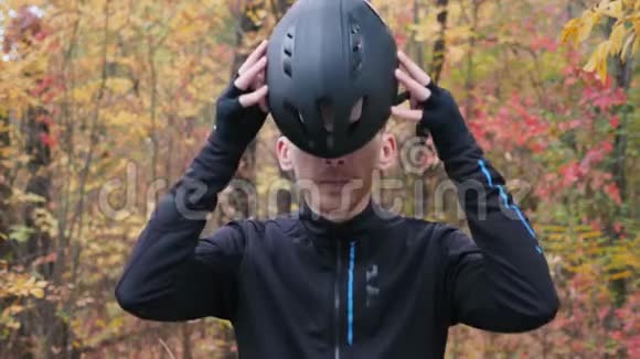 年轻的男运动员穿着黑色自行车服装站在秋季公园戴上黑色头盔自行车的概念男子骑自行车视频的预览图