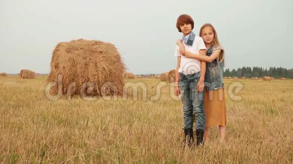 年轻夫妇在干草堆背景下的收获场上拥抱拥抱在农村摆姿势的少年女孩和男孩视频的预览图
