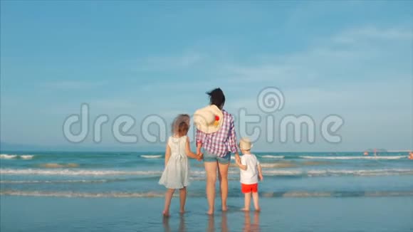一个幸福家庭的剪影站在海滩上在日落时看着大海有孩子的快乐妈妈视频的预览图