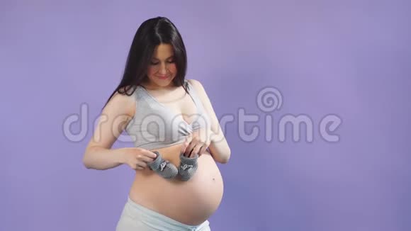 一位孕妇抱着婴儿小鞋靠近她的大肚子的肖像视频的预览图