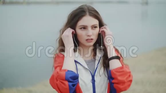 年轻女子戴着耳机进行有氧训练背景是河流或海洋视频的预览图