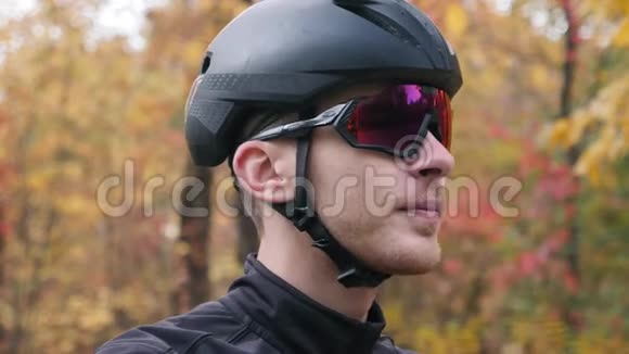 年轻英俊的职业三项运动员戴着黑色头盔和自行车手套在秋季公园摘下运动眼镜的肖像额外费用视频的预览图