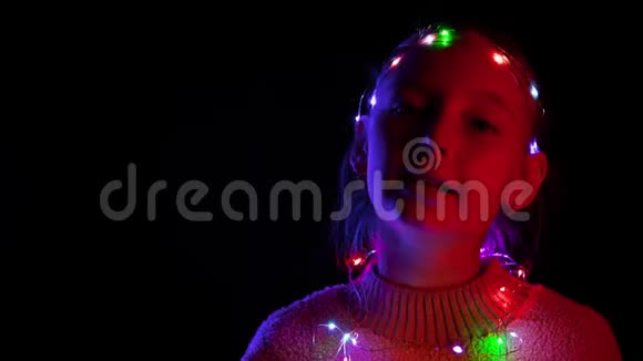 快乐的少年女孩在发光的圣诞花环在黑暗的工作室跳舞戴着霓虹花环的快乐女孩视频的预览图