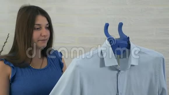 一个年轻的女人在电话里说话用蒸汽抚摸男人衬衫蒸衣服蒸的过程蓝色视频的预览图