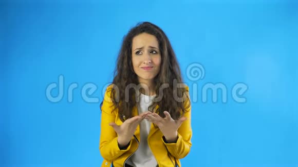 迷糊的年轻女子穿着黄色夹克在工作室蓝色背景视频的预览图