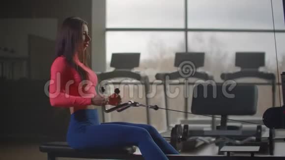 健身房专用训练机的动力训练坐着的女人在背景下拉动模拟器的重量视频的预览图