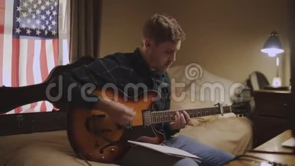 专心致志的年轻人坐在床上弹吉他在家写音乐视频的预览图
