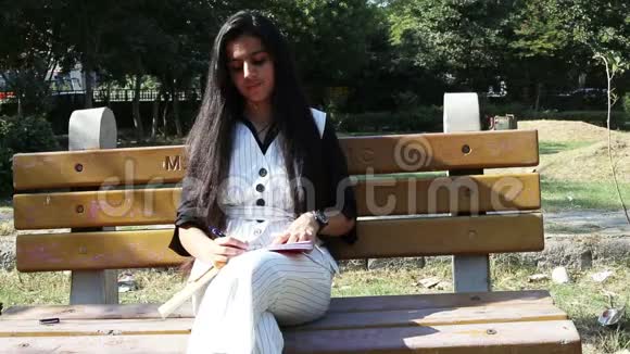 使用智能手机的少女她坐在公共公园里视频的预览图
