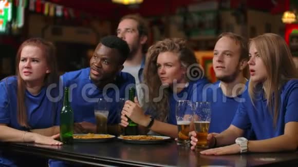 一群穿着蓝色t恤的男女球迷在酒吧里欢呼喝啤酒非裔美国人和视频的预览图