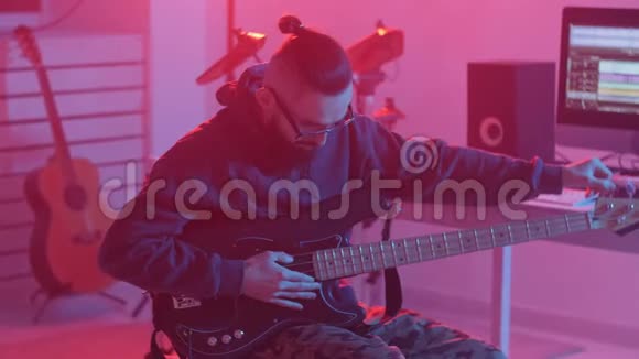 爱好和制作音乐的概念一个留胡子的年轻人在一家音乐工作室里弹低音吉他视频的预览图