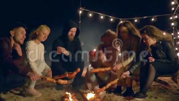 海滩晚餐朋友晚上在沙滩篝火上用灯光做饭视频的预览图