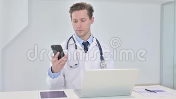 有魅力的年轻医生在办公室讲智能手机视频的预览图