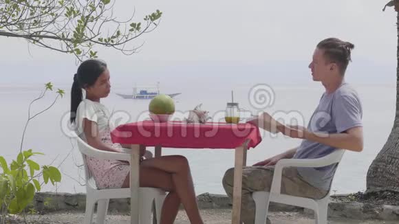 男人和女人坐在一张桌子旁在靠近海洋的咖啡馆里交谈视频的预览图