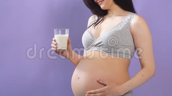 孕妇身材苗条穿着内衣大肚子手里拿着一杯牛奶隔在蓝墙上视频的预览图