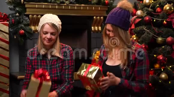 两个穿着红衬衫戴着滑稽帽子的滑稽少女坐在新年或圣诞树旁听不懂视频的预览图