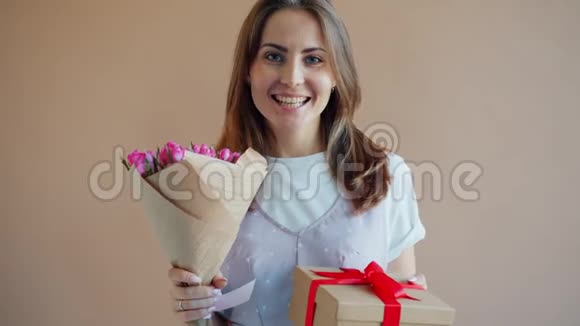 以米色背景为背景的带花和礼品盒的幸福年轻女士肖像视频的预览图