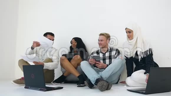 由两名男子和两名混血妇女组成的负责任的年轻创意办公室组的正面视图坐在地板上和视频的预览图