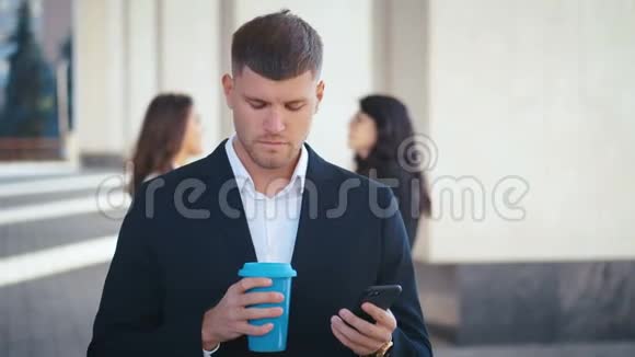 男性商人使用智能手机应用程序在城市办公室外面发短信喝咖啡或茶穿着视频的预览图