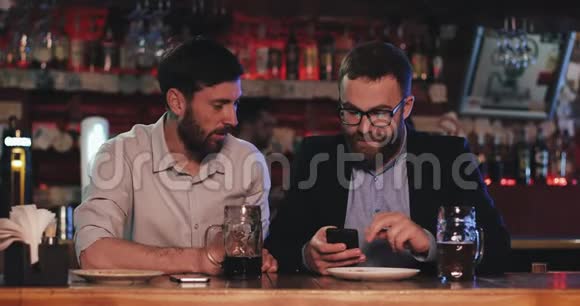 两个有智能手机的老朋友晚上在啤酒酒吧聊天视频的预览图