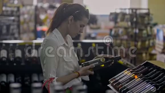有魅力的年轻女人选择葡萄酒站在超市的酒精区视频的预览图