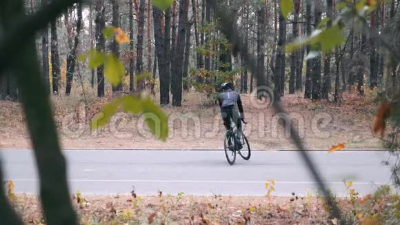 英俊的职业男性自行车手黑色头盔和运动太阳镜在秋季森林的道路自行车上玩得很开心年轻男子视频的预览图