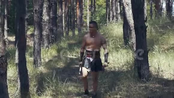 肌肉发达的野蛮人手里拿着两把斧头在森林里散步视频的预览图