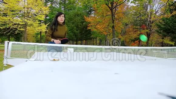 一个快乐的女人在公园打乒乓球或乒乓球秋天视频的预览图