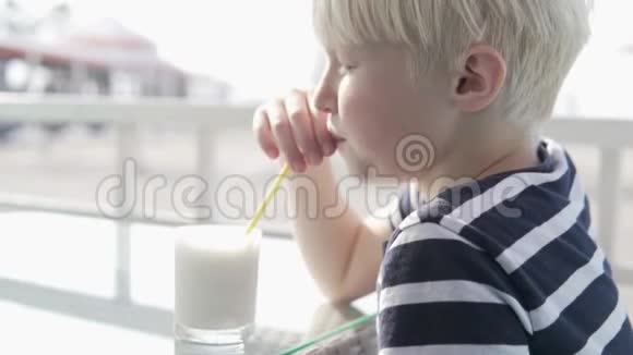 可爱的金发男孩在炎热的夏天在咖啡馆里喝奶昔视频的预览图