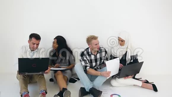 在白色办公室里坐在地板上的愉快聪明有目的的混合种族公司同事的正面景色视频的预览图