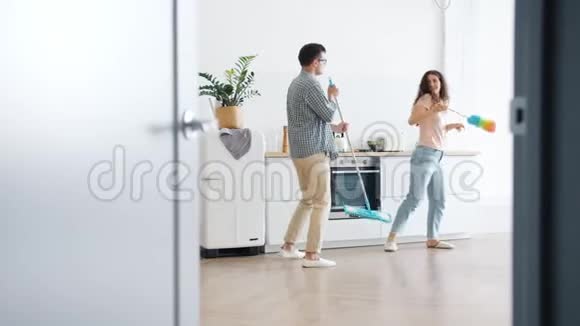 男人和女人在家里的厨房里用拖把和掸子跳舞的慢动作视频的预览图