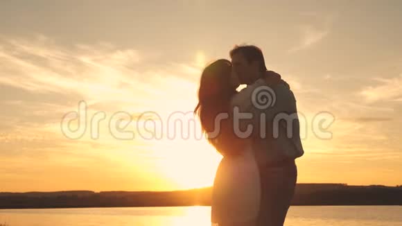 快乐的男人和女孩在海滩上日落时亲吻和拥抱爱的男人和女人在浪漫的夕阳下视频的预览图