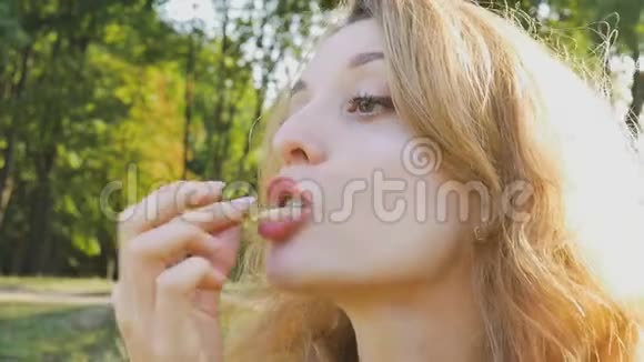 在公园里坐在长凳上吃炸薯条的年轻金发女人的户外肖像不健康饮食视频的预览图