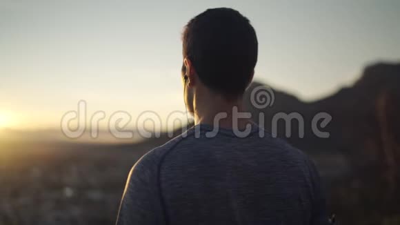从山顶欣赏清晨日出的男子听音乐看城市的后景视频的预览图