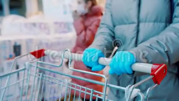 穿着蓝色橡胶手套的女人正在超市推一辆手推车把手举起来视频的预览图