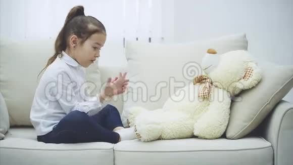 可爱的小女孩坐在沙发上和她的泰迪说话拼命地弯曲手指摇动泰迪视频的预览图
