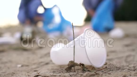 特写塑料碎片落在沙滩上背景模糊的志愿者视频的预览图