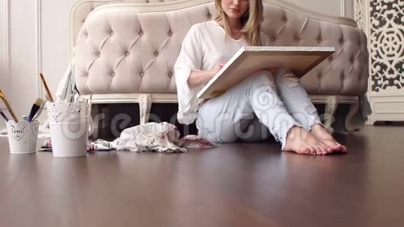 穿着破牛仔裤和白衬衫的性感女孩坐在地板上的家里视频的预览图