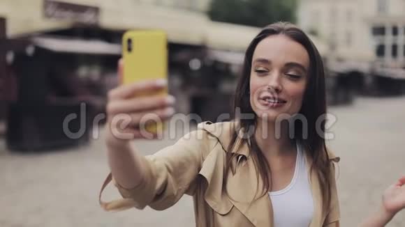 美丽快乐的年轻女孩打着视频电话举着电话微笑着站在城市街道上视频的预览图