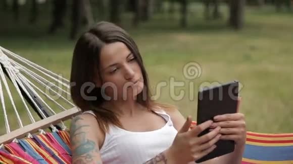 女孩躺在吊床上手里拿着一块平板电脑在森林背景上视频的预览图