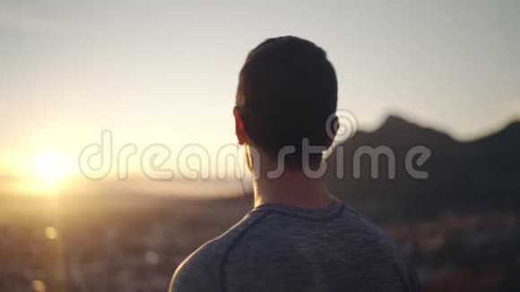 一位健身男子使用耳机听音乐的侧视清晨可俯瞰城市景观视频的预览图